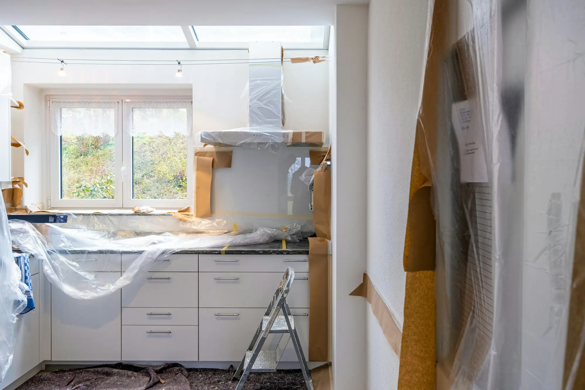 A kitchen mid-restoration with cabinets and counters covered in protective plastic